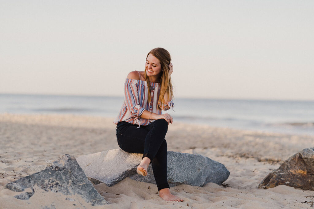 Girl touching hair and sitting on rock smiling at Cape Henlopen State Park in Delaware